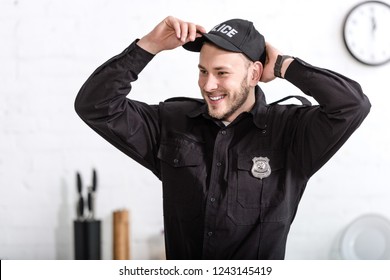 Handsome Police Officer Smiling And Putting On Cap At Kitchen