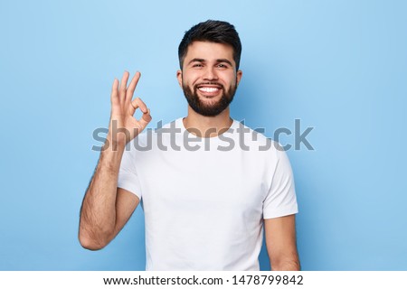 handsome positive bearded man in white T-shirt isolated on blue background showing ok sign.close up portrait, body language, everything is ok, allright. people and success concept. successful business