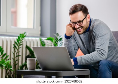Handsome positive and cheerful man with glasses smiling looking for a date on laptop at home. Freelancer or informal businessman, work from home.  - Shutterstock ID 1323788582