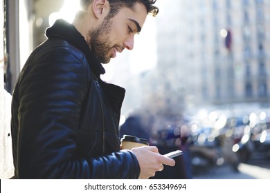 Handsome Positive Tourist Searching Interesting Places To Visit In New City While Standing At Spring Street.Bearded Hipster Guy In Good Mood Enjoying Free Time With Modern Device And Aroma Coffee