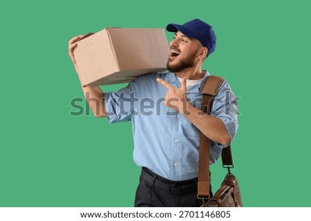 Handsome postman pointing at parcel box on green background