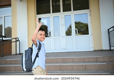 Handsome Primary School Student, Boy, Child, Kid Standing On The Stairs In Front Of A School Building Waving Goodbye Looking Back Over His Shoulder
