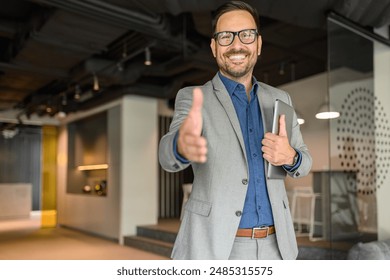 Handsome professional with laptop smiling and offering handshake while welcoming client in office - Powered by Shutterstock