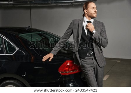 handsome professional with ponytail posing next to his car and looking away, business concept