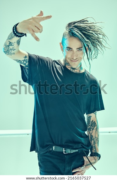 A handsome punk
rock musician with dreadlocks in stylish black clothes  posing
among neon lamps on a light background. Space punk rock music.
Youth alternative culture. 