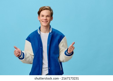 a handsome red-haired guy stands in a fashionable blue bomber jacket joyfully showing two thumbs up