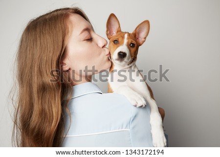 Handsome redhead hair young female hugging and kissing her puppy basenji dog. Love between dog and owner. Isolated on white background.