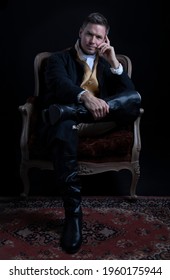 Handsome Regency gentleman sitting in a red velvet chair in a darkened room