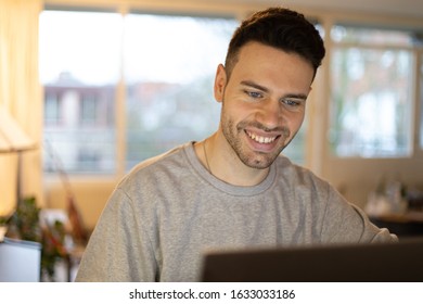 Handsome And Relaxed Young Man With A Genuine Smile Is Enjoying Working On His Laptop From Home. 