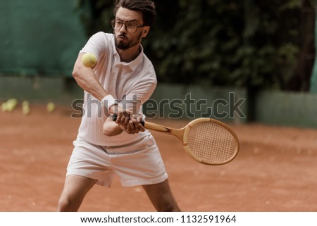 handsome retro styled tennis player hitting ball at tennis court