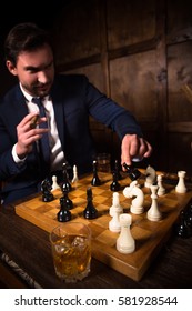 Handsome rich executive man playing chess and smoking expensive cigar. Glass with whiskey. Business concept. Restaurant atmosphere.