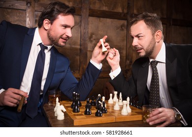 Handsome rich men playing chess all together in expensive restaurant or cafe. Rich men sitting face to face demonstrating competition between their enterprises, companies or firms.