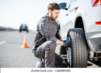 Handsome Road Assistance Worker In Uniform Changing Car Wheel On The Highway