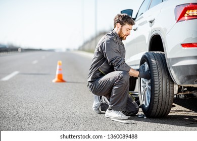 Handsome road assistance worker in uniform changing car wheel on the highway - Shutterstock ID 1360089488