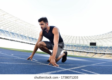handsome runner in start position on running track at stadium