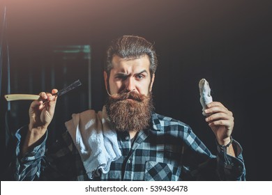 Handsome Sad Man, Bearded Hipster, Brunette With Long Beard And Moustache Shaves With Open Vintage Razor With Blade And Shaving Brush On Dark Background