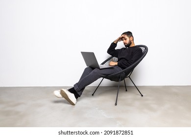 Handsome Sad Man Working On Laptop And Smiling While Sitting In Big Comfortable Chair At Home