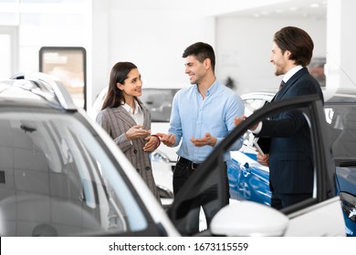 Handsome Sales Consultant Showing Young Couple New Luxury Auto, Happy Spouses Discussing Their Choice