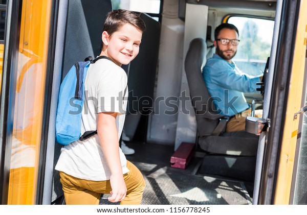 handsome school bus driver and schoolboy looking\
at camera