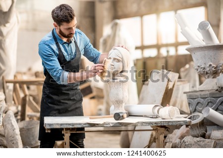 Handsome sculptor brushing sculpture of the woman's head at the working place in the old atmospheric studio
