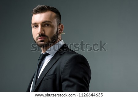 handsome security guard with security earpiece looking at camera isolated on grey