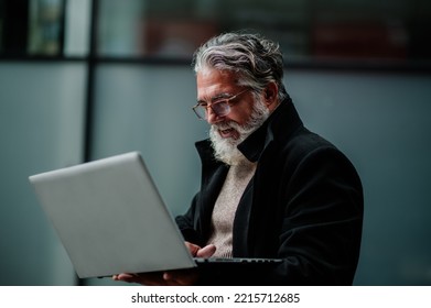 Handsome Senior Businessman With White Beard And In Formal Outfit Using Laptop While Sitting Outside. Close Shot Of A Elderly Man Using Computer Outside. Copy Space.