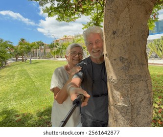 Handsome senior cheerful couple embrace in the park looking at camera taking a selfie with a selfie stick - Powered by Shutterstock