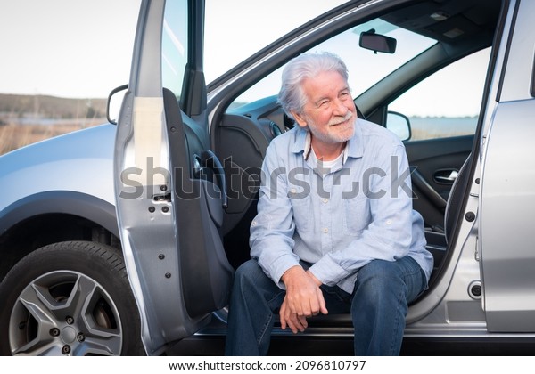 Handsome senior driver man sitting in his car\
relaxing smiling looking\
away