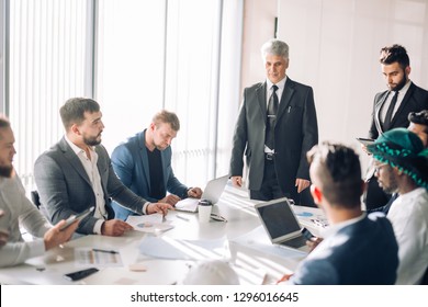 Handsome Senior Grey-haired Caucasian Executive Leading The Meeting Of International Partners In Boardroom, Having Positive Mood And Introducing The New Board Member To His Colleagues