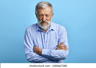 Handsome senior man in blue shirt with skeptic, nervous expression standing with crossed arms. close up portrait. isolated light blue background