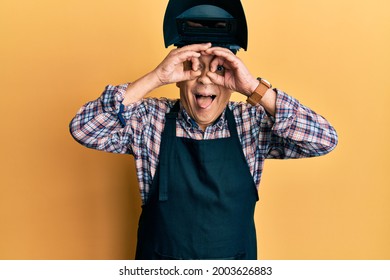 Handsome senior man with grey hair wearing welding protection mask doing ok gesture like binoculars sticking tongue out, eyes looking through fingers. crazy expression.  - Powered by Shutterstock