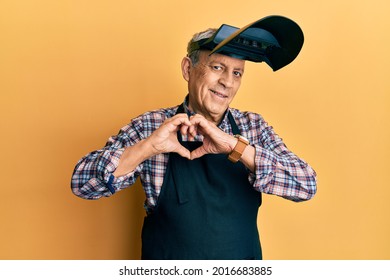 Handsome senior man with grey hair wearing welding protection mask smiling in love doing heart symbol shape with hands. romantic concept.  - Powered by Shutterstock