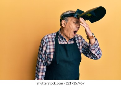 Handsome Senior Man With Grey Hair Wearing Welding Protection Mask Surprised With Hand On Head For Mistake, Remember Error. Forgot, Bad Memory Concept. 