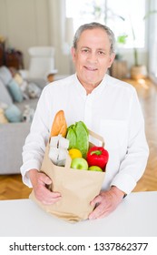 Handsome Senior Man Holding Paper Bag Full Of Fresh Groceries And Smiling At Home