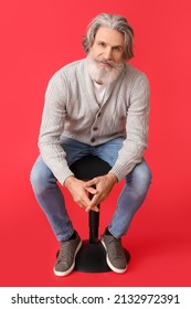 Handsome Senior Man In Knitted Sweater Sitting On Chair Against Red Background