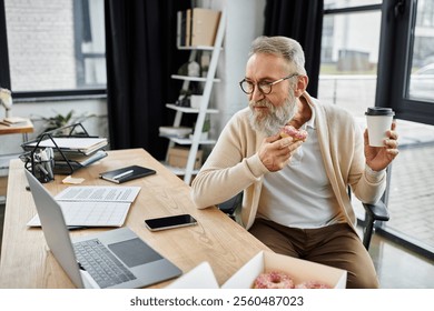 Handsome senior man relaxes with a donut and coffee while engaged with his laptop at work. - Powered by Shutterstock