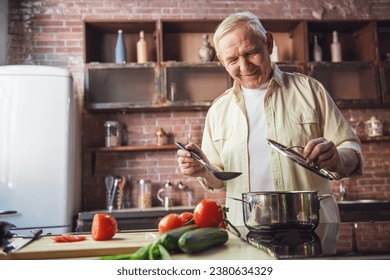 Handsome senior man is smiling while cooking in kitchen - Powered by Shutterstock