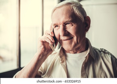 Handsome Senior Man Is Talking On The Mobile Phone And Smiling While Standing In Kitchen