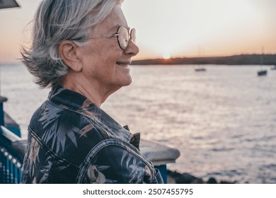 Handsome senior woman at the sea port enjoying free time and relax at sunset light. Elderly caucasian lady on travel or retirement - Powered by Shutterstock