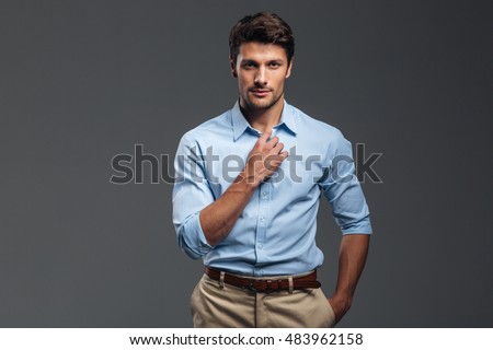 Handsome serious man buttoning his shirt isolated on a gray background [[stock_photo]] © 