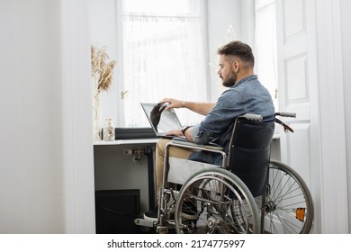 Handsome Serious Man In Wheelchair Finishing His Remote Work And Closing Modern Laptop At Home Office. Concept Of Freelance, Temporary Disability And Technology.