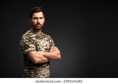 Handsome serious soldier holding arms crossed wearing military camouflage t shirt looking at camera isolated on black background - Powered by Shutterstock