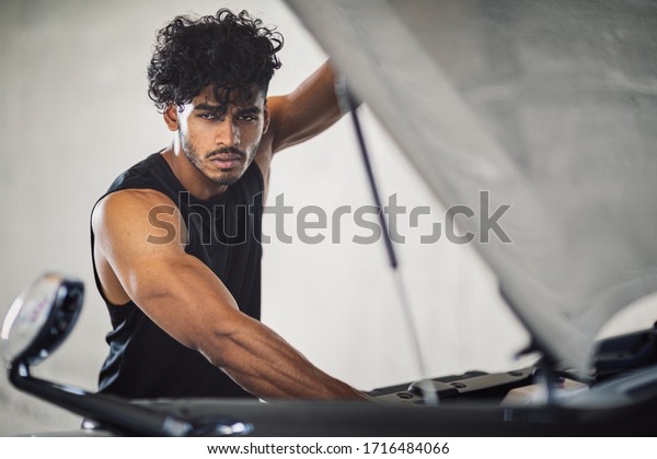 A\
handsome and sexy arabian or indian male model with big muscles and\
a good body and a cute face with curly brown hair, is a repairman\
of a car and watching under the bonnet to the\
engine