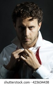 Handsome sexy man with curly hair and unshaven face in white shirt and red untied bow on black background