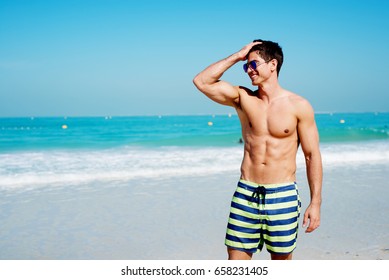 Handsome shirtless muscular fitness man at the beach, looking aside and smiling. - Powered by Shutterstock