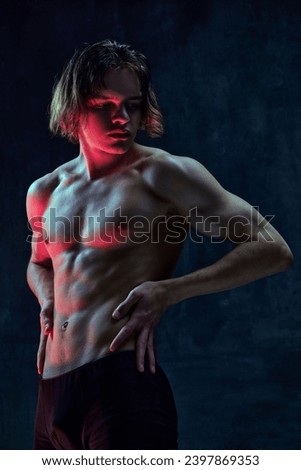 Handsome shirtless young guy with relief, muscular, fit body shape standing shirtless against dark textured studio background. Concept of men's beauty, health, body art and aesthetics, care, sportive