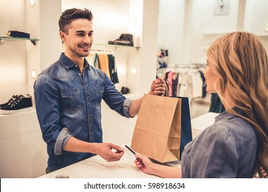 Handsome shop assistant is smiling while giving purchases and credit card to beautiful client