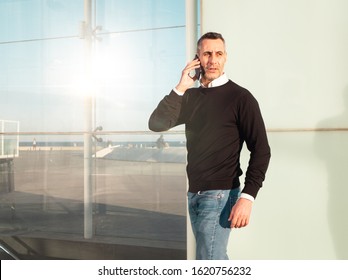 Handsome Silver Fox Man Talking On Mobile Phone With Glass Office Building In Background 