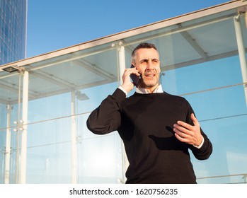 Handsome Silver Fox Man Talking On Mobile Phone With Glass Office Building In Background 