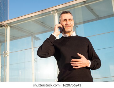 Handsome Silver Fox Man Talking On Mobile Phone With Glass Office Building In Background 